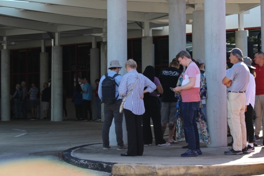People stand in line under a covered awning at a polling location.