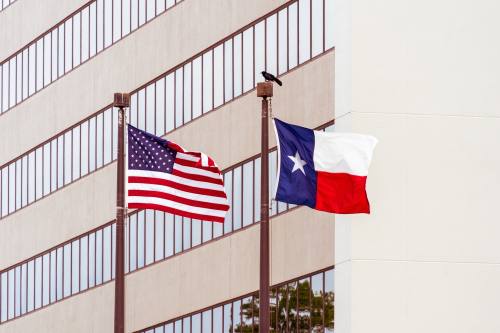 The U.S. and Texas flags wave in front of a tan and white building
