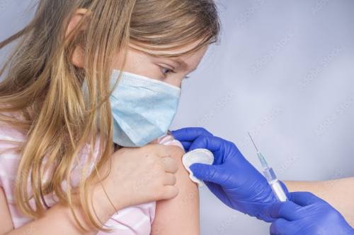A blond child wearing a mask receives a vaccine.