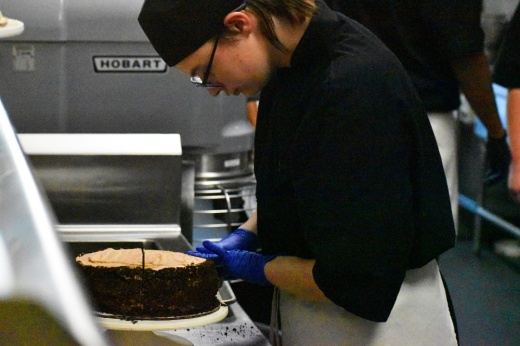 Byron Bistro and Byron Nelson High School student Connor Masure cuts a chocolate cake. (Cody Thorn/Community Impact)