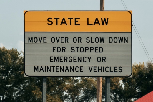 A yellow and white road sign reads 'move over or slow down for stopped emergency or maintenance vehicles."