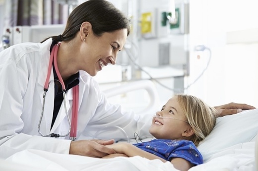 A doctor with dark hair smiles at a blond child in a hospital.