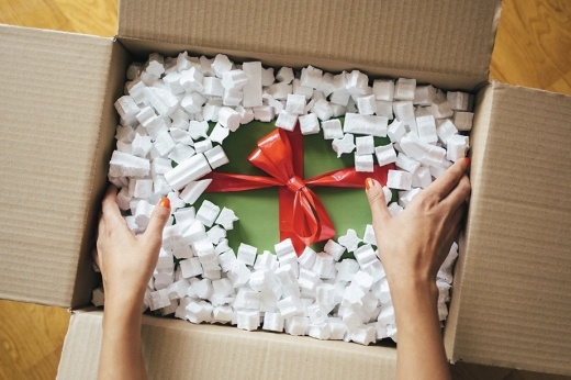 A light-skinned person opens a box with a red and green package inside.