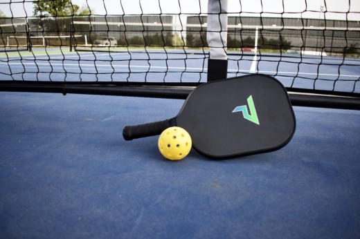 pickleball paddle and yellow ball placed on a blue court in front of a net