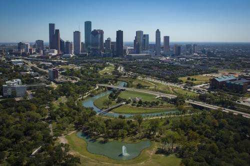 This is a picture of the Houston skyline in the distance with trees and green spaces in the foreground.