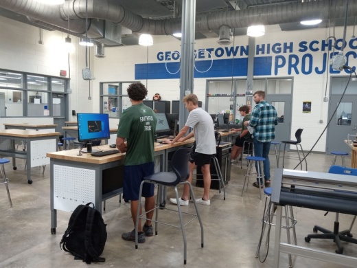 students in the drone program stand at their desks working on their laptops