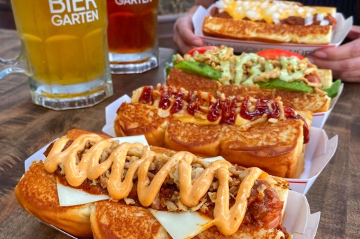 Hots dogs on paper trays with beer in the background.