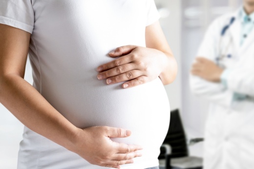 A pregnant woman wearing a white shirt with a doctor standing behind her.