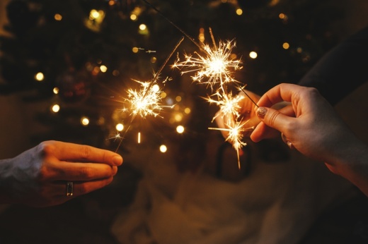 Hands holding fireworks against Christmas lights in a dark room. (Photo courtesy of Adobe Stock).