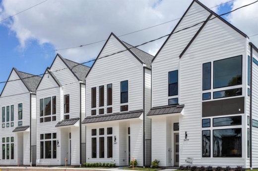 This shows four white townhomes next to each other with angular roofs and large windows.