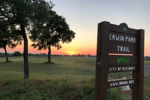 Erwin Park trails sign in front of a tree and a sunset.