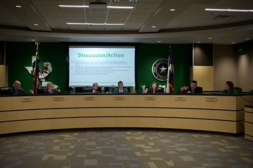 seven people sit behind a large wood dais at a school board meeting