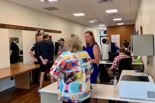 Two women standing and talking inside a room of other people.