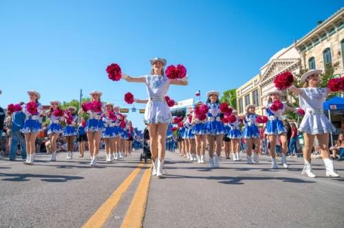 cheerleaders with red pom poms and blue outfits walk along the streets of georgetown dancing