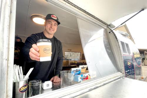 employee hands coffee to camera out of food truck 