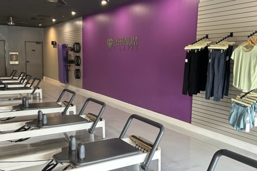 Pilates studio with reformer machines, a purple wall and hanging clothes racks
