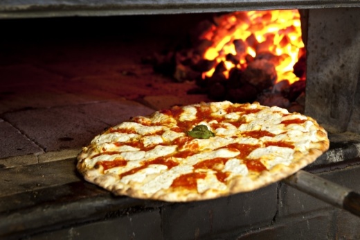 pizza being placed into a brick oven