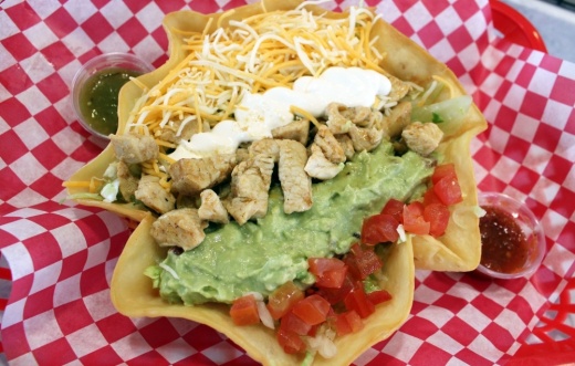 large crispy taco shell filled with chicken, fresh lettuce, tomatoes, cheese, sour cream and guacamole on a red and white checked background