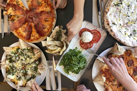 several plates with pasta, cheese, tomatoes and salad are on a table as people with forks grab the food