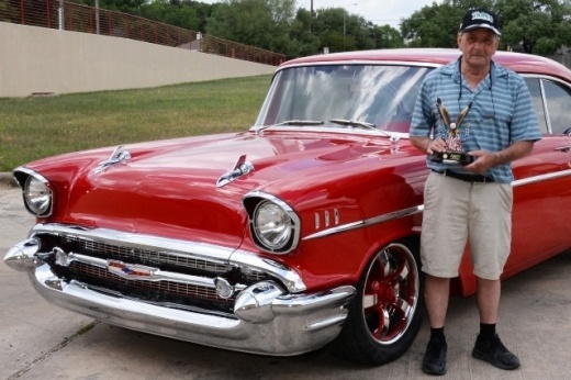 A man holding a trophy stands in front of his car.