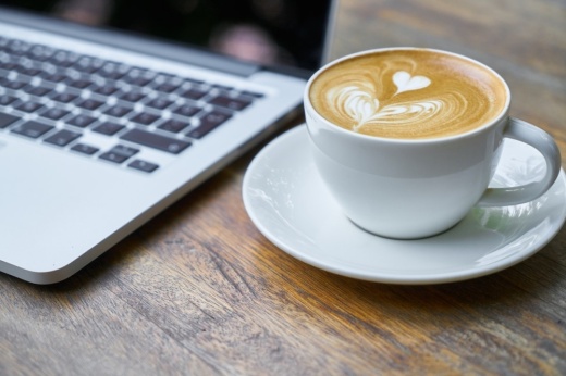 latte with foam art on a saucer next to a laptop