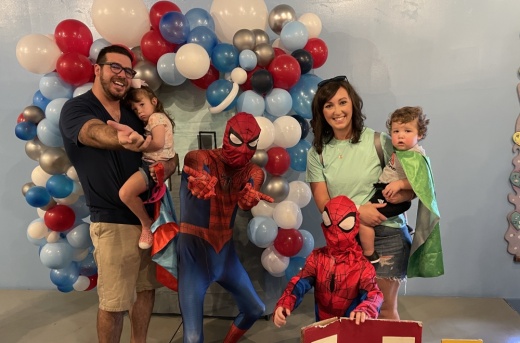 Spider-Man poses with a family and balloons.