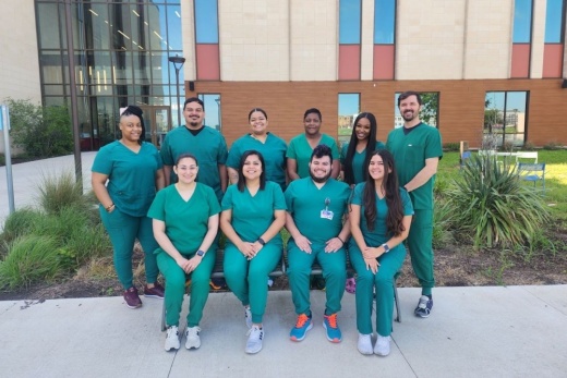 Ten health care graduates pose for a photo outside on a sunny day