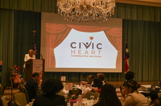 someone speaks at a podium next to a projectors screen that says civic heart