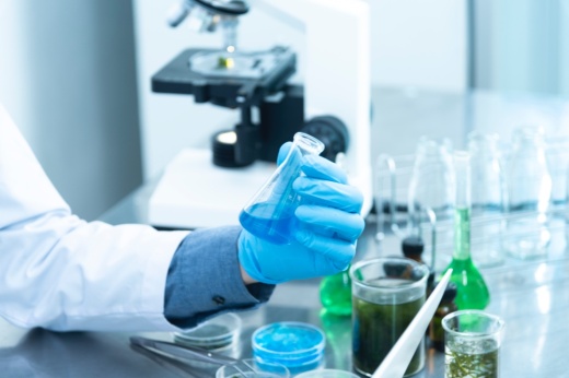 gloved hand holding a liquid substance in a glass container in a lab