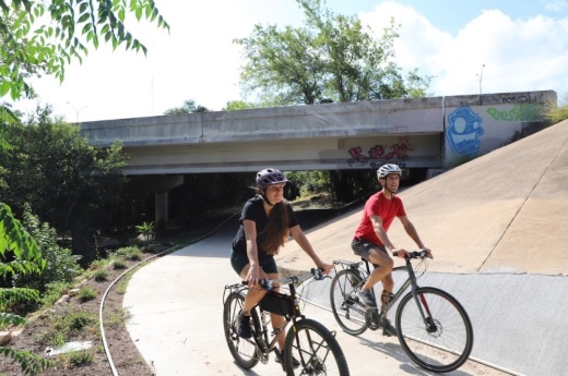 Two people on bikes ride through the Violet Crown Trail on a sunny day.