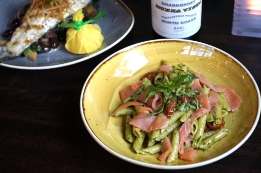 A yellow dish with pasta and slices of meat and a blue dish with cooked fish