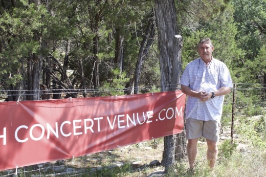 Man poses on property with banner that reads "Stop Fitzhugh Concert Venue."