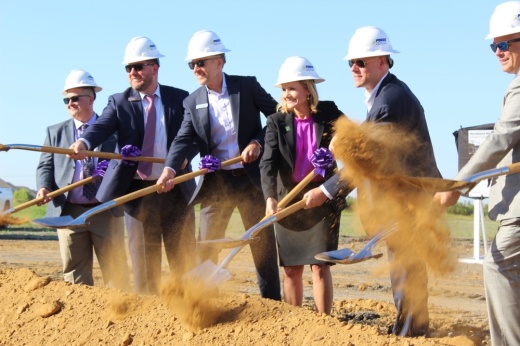 a woman and men in suits and hardhats dig shovels into dirt