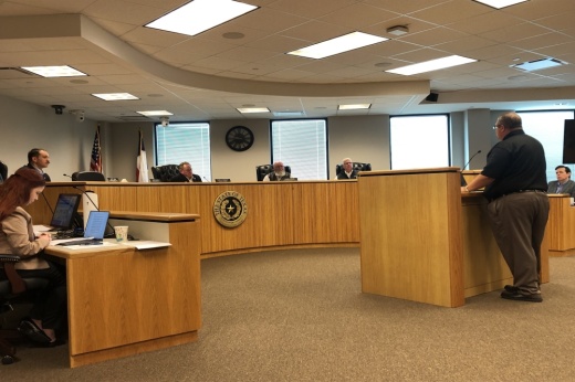 A meeting is held in a room with a dais and a person at a podium.