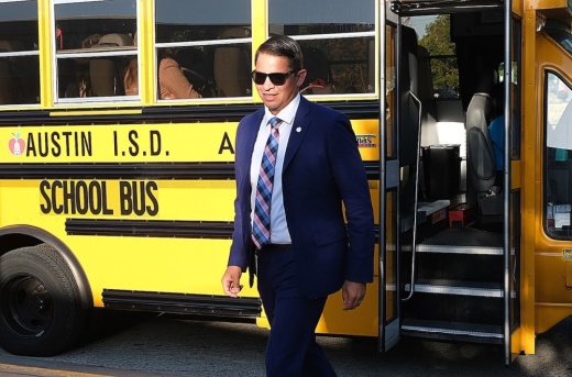 A man exits a school bus for Austin ISD wearing a suit and sunglasses.