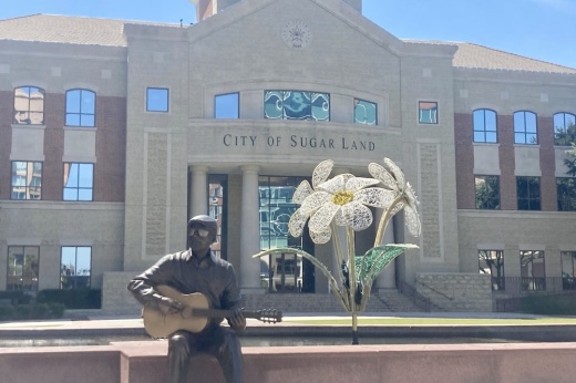 Statue of man playing guitar and a metal flower in front of Sugar Land City Hall