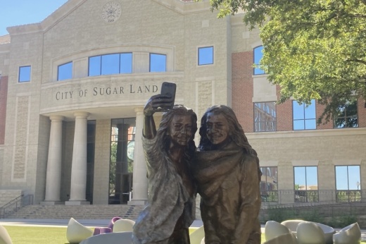 A statue of two girls taking a phone selfie picture in front of Sugar Land City Hall and Town Center