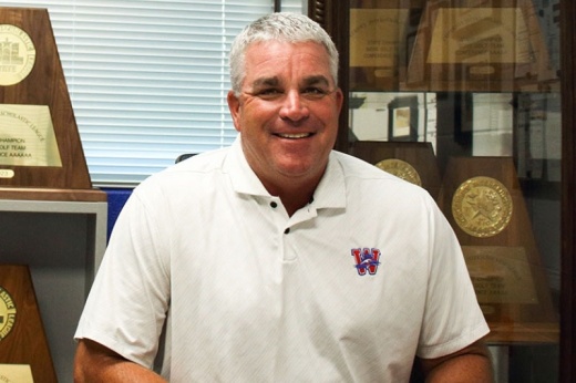 A photo of Athletic Director Callan Nokes standing in front of a trophy case
