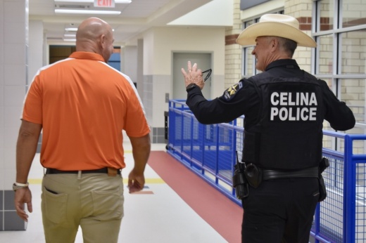 a man in a polo shirt and khaki pants walks down the hall next to a police officer in a cowboy hat