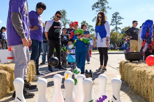 Children in costumes play a bowling game outside.