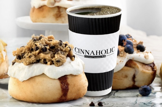 2 large cinnamon rolls with blueberry toppings and icing next to a large cup of coffee