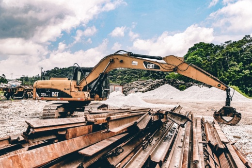 Construction equipment picking up steel beams during daytime with clouds and trees in background