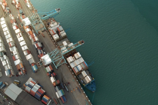 Aerial view of shipping container boat loading containers at a shipping port with green water