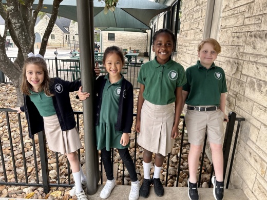 Four young students smile outside at school.