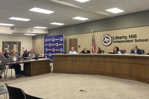 liberty hill isd board of trustees on the dais listen to dee carney sitting at a table adjacent to the dais