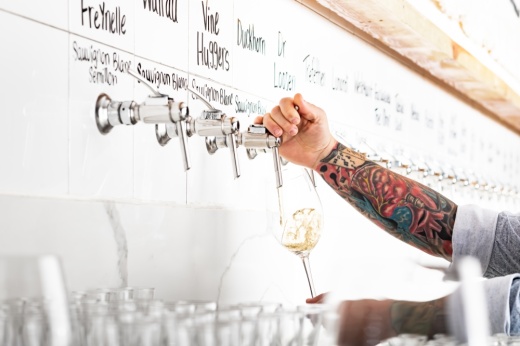 A person pours a glass of white wine from the tap wall.