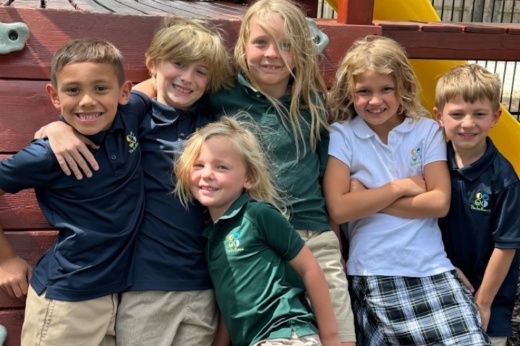 Six children smile and pose for a photo outside at the school.