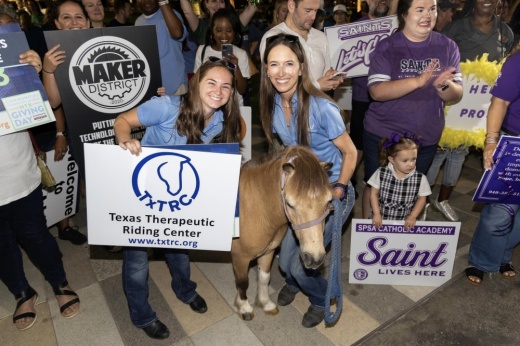 Several people holding signs, focused on two smiling white women with a miniature horse