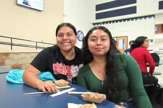 Two students smile while eating food.