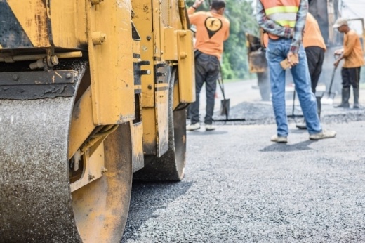 Road flattening machine at construction site with workers pouring tar on a road in the background